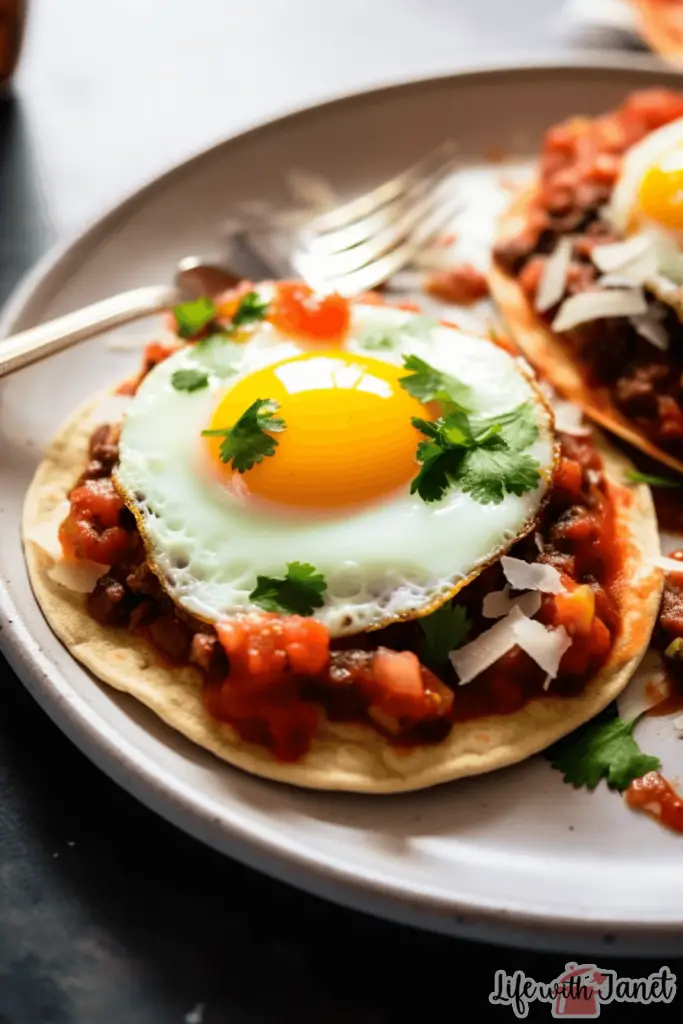 Overhead view of Huevos Rancheros with sunny-side-up eggs, sliced avocados, and a dash of spicy salsa.