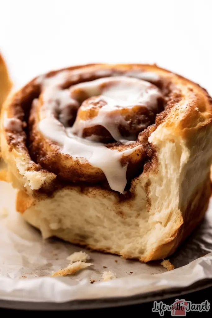 Stack of buttery overnight cinnamon rolls beside a bowl of tangy cream cheese frosting.