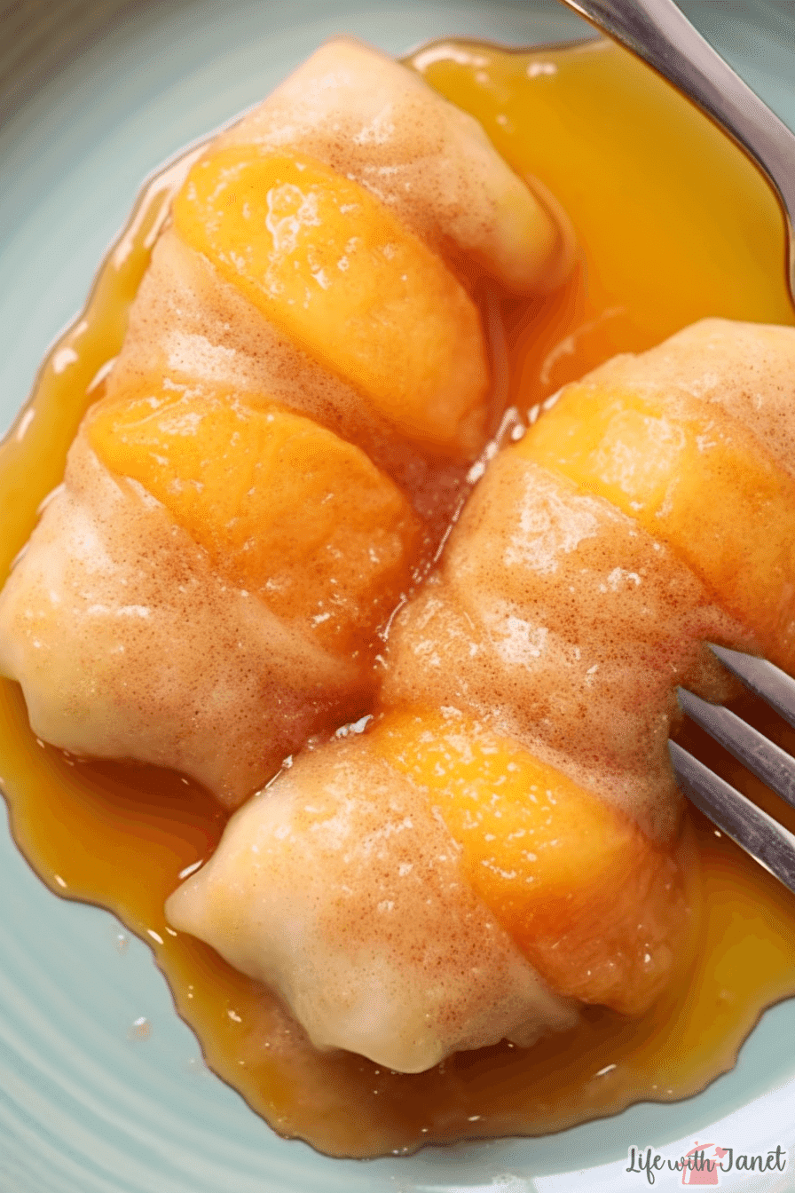 Golden-brown peach dumplings on a white plate with a scoop of vanilla ice cream, garnished with fresh mint leaves.